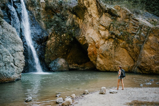 person looking at a waterfall as they stand on little beach